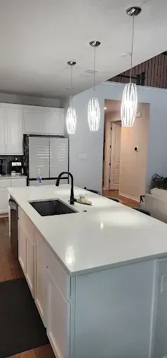 Modern kitchen with a white island, black sink faucet, pendant lights, and open doorway.