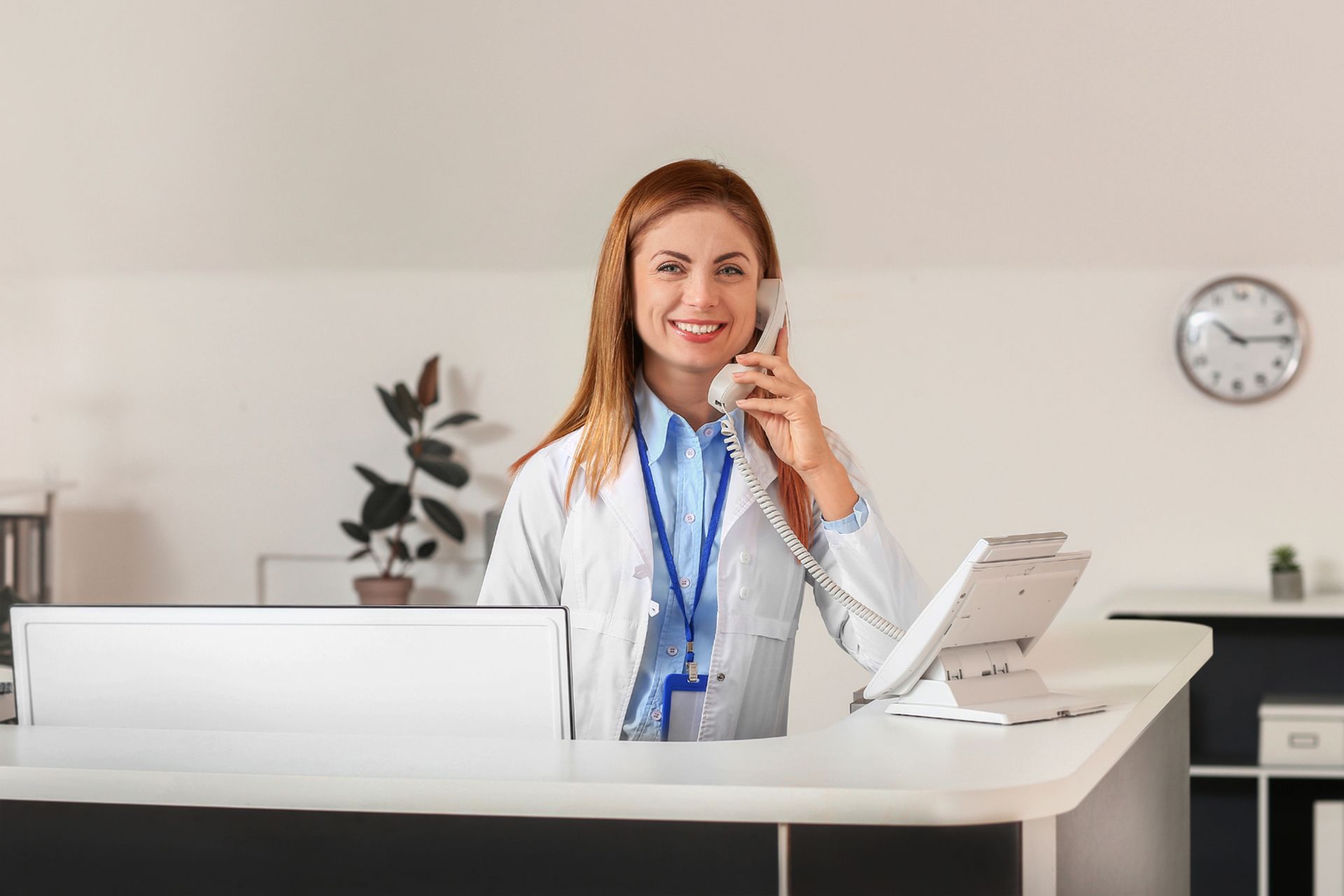 a female doctor is talking on a cell phone at a reception desk .