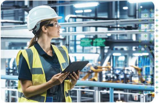 an occupational health specialist in a hard hat and safety vest is holding a tablet in a factory .