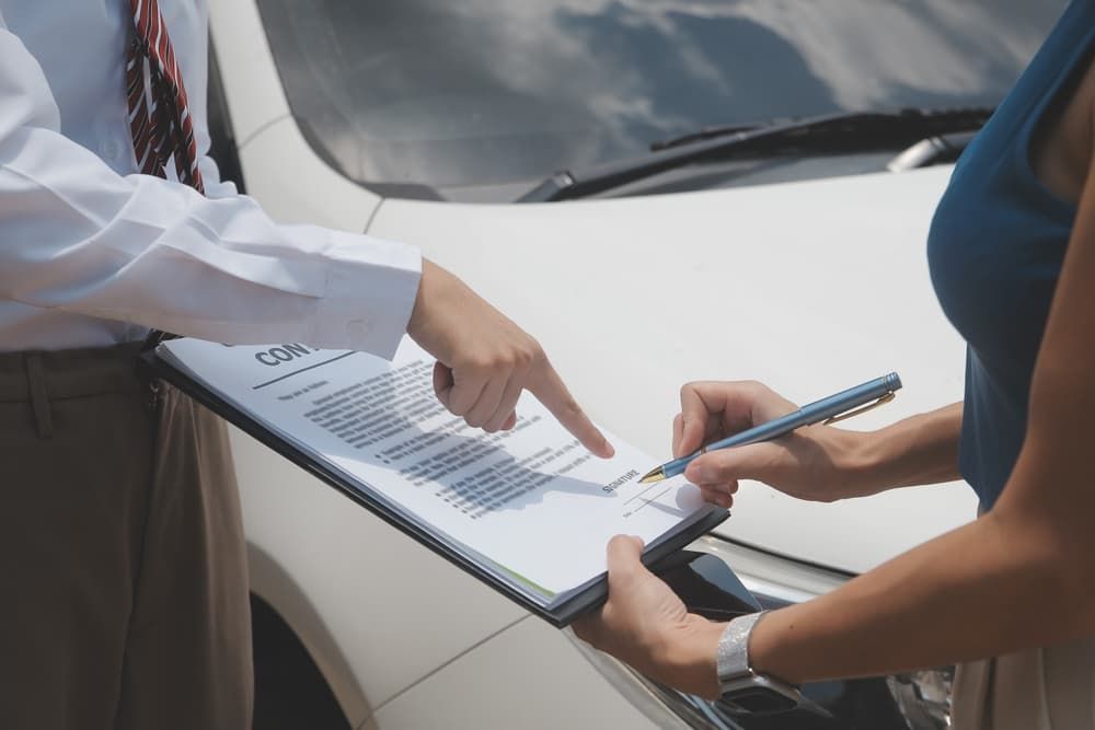 Side view of writing on clipboard while insurance agent examining car after accident