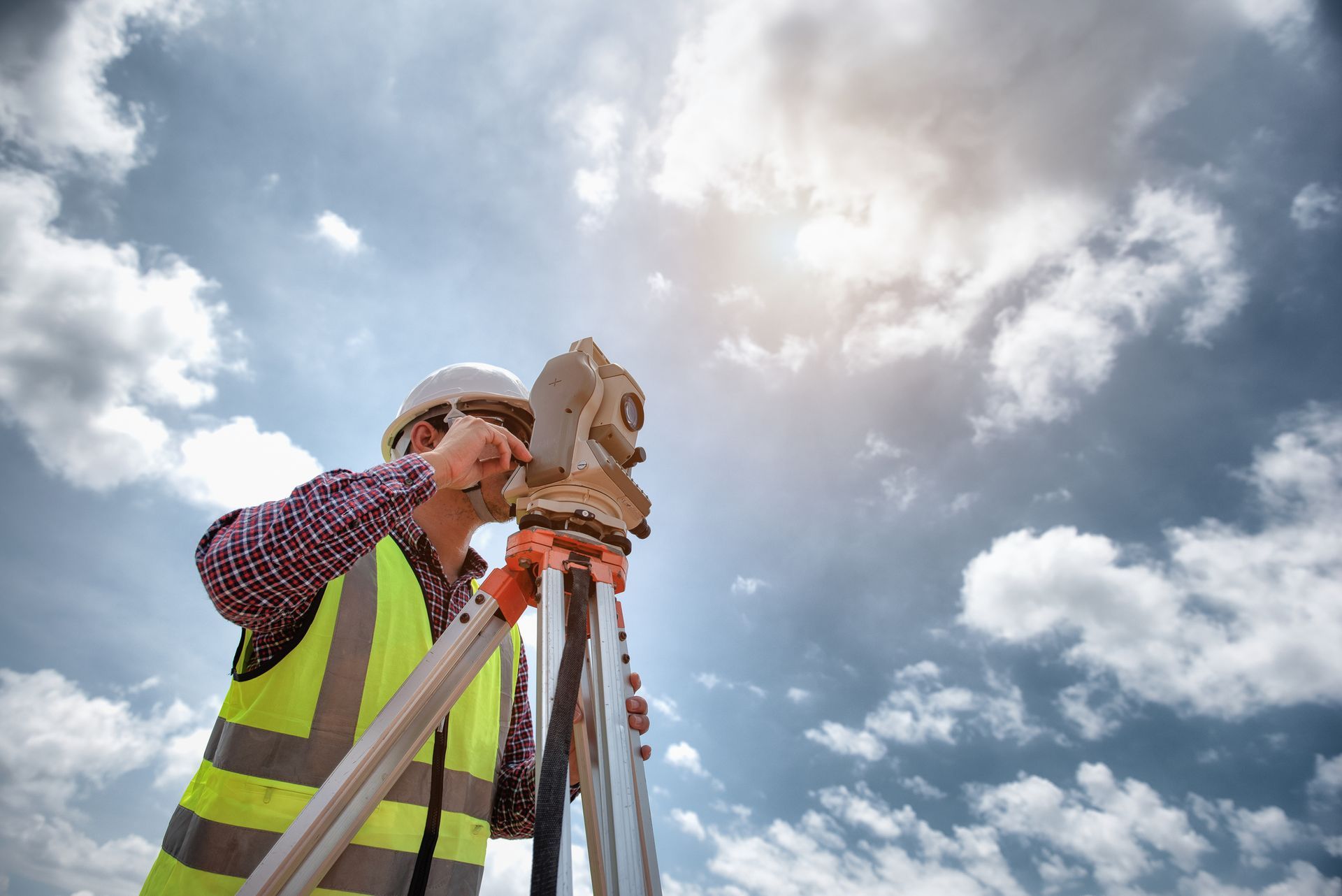 A construction worker is using a theodolite on a tripod.