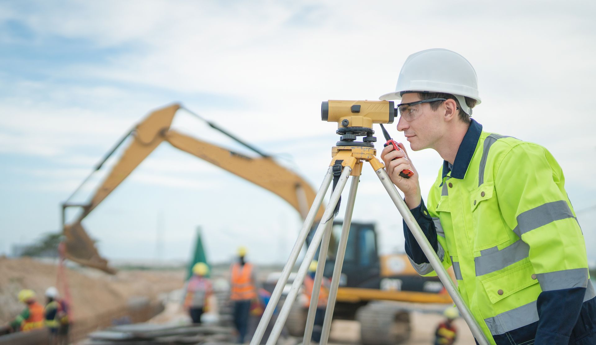 A construction worker is using a level on a tripod and talking on a walkie talkie.