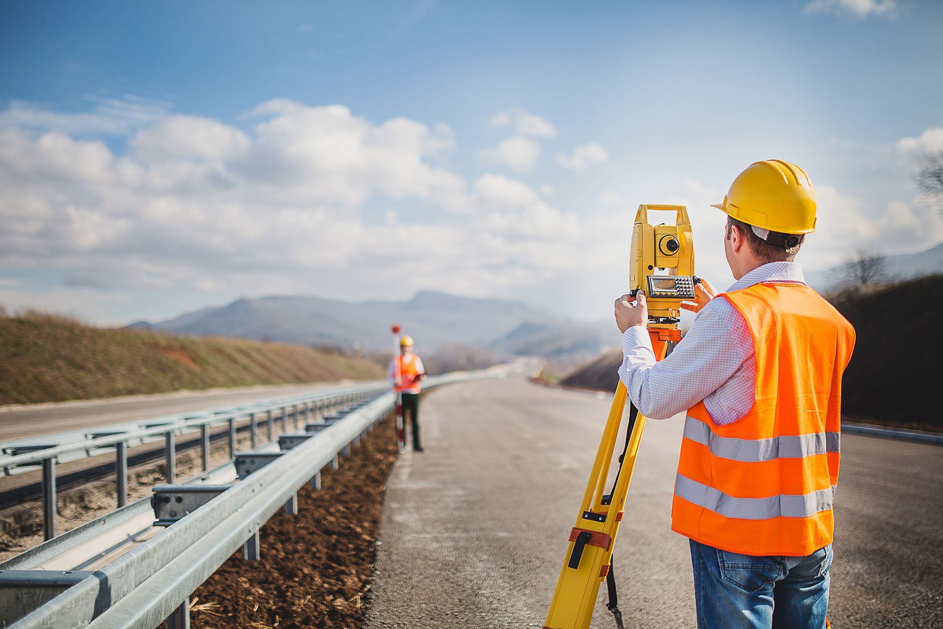 A man is standing on the side of a road using a theodolite.