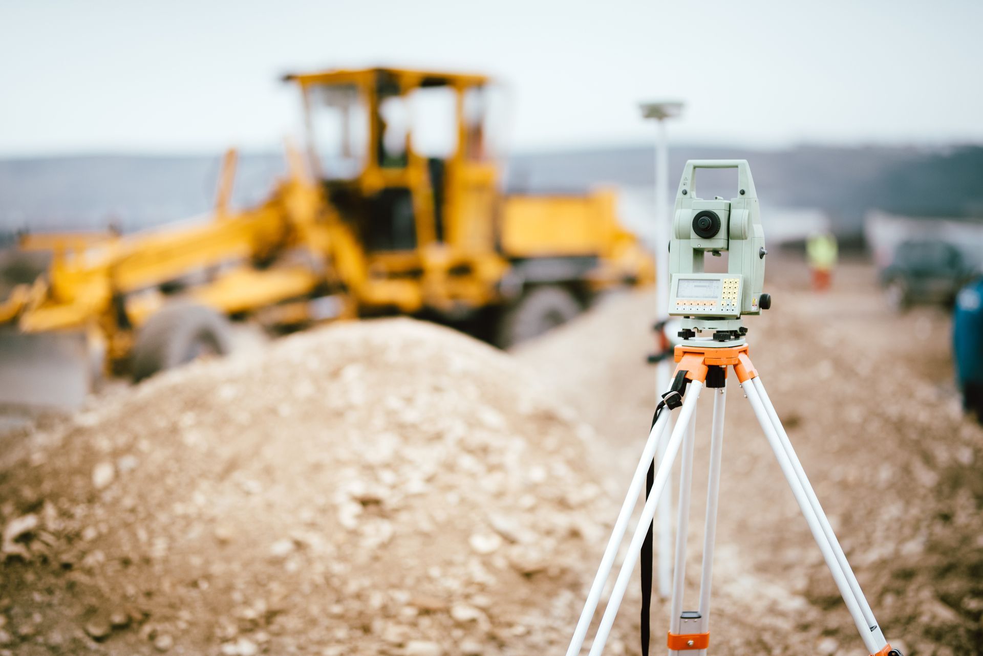 A theodolite is sitting on a tripod at a construction site with a bulldozer in the background.