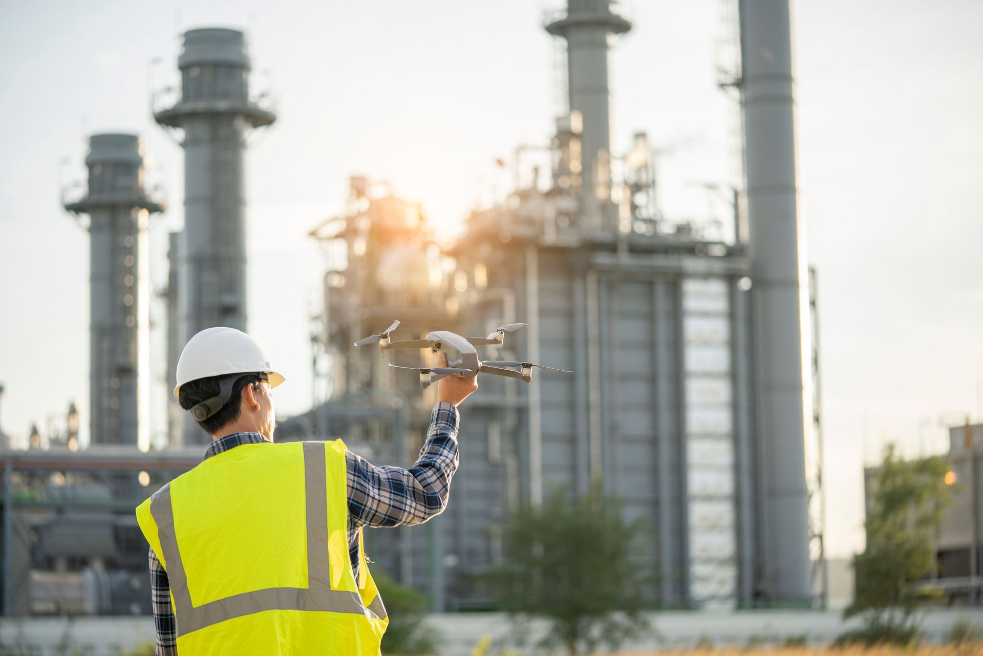 A man in a yellow vest is standing in front of a factory holding a wrench.