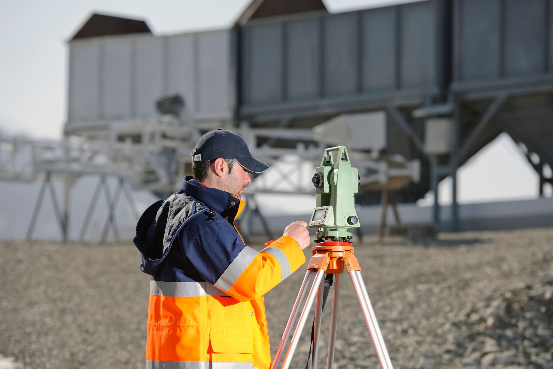 A man in an orange and blue jacket is working on a tripod.