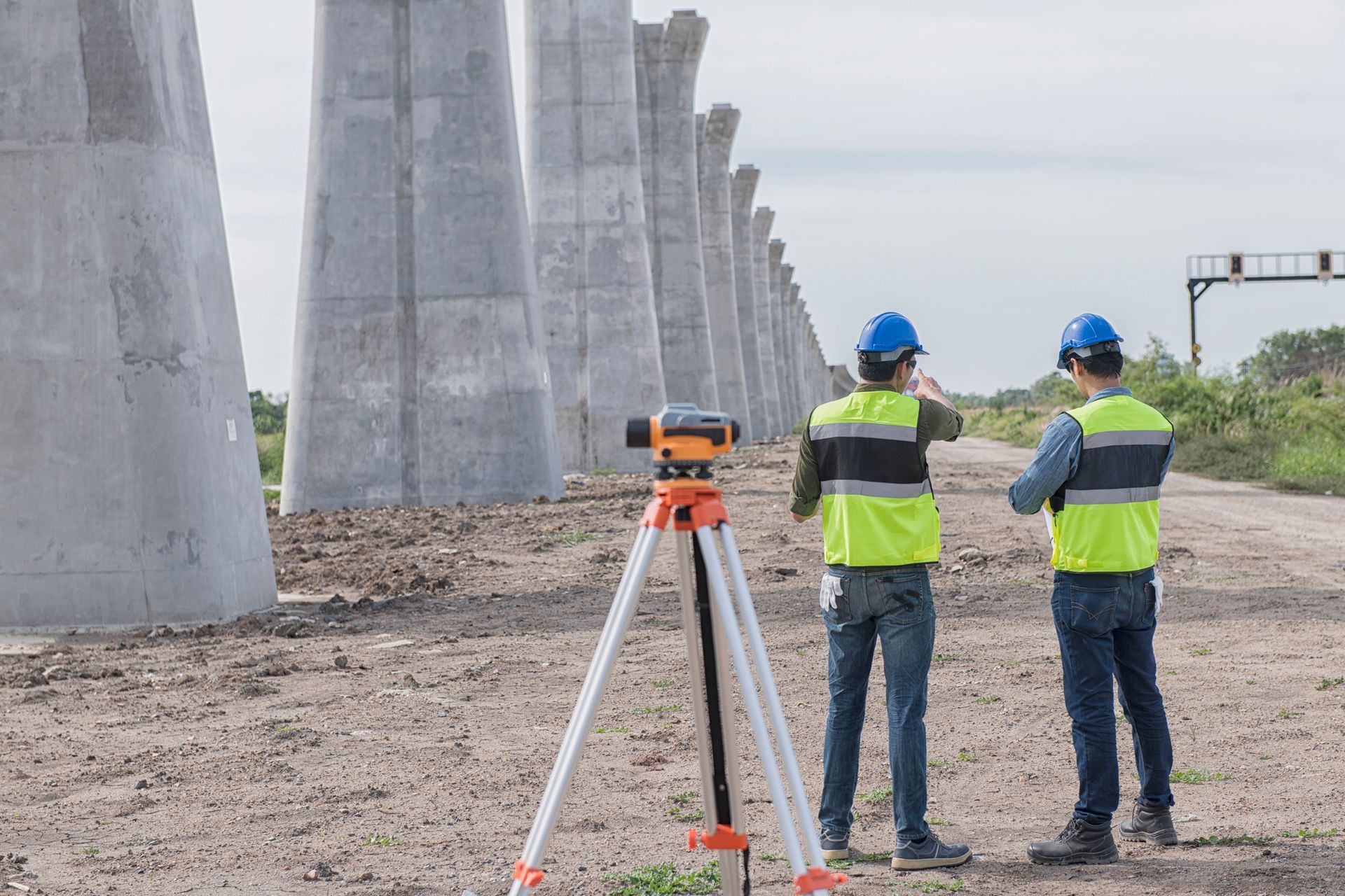 Two construction workers are standing in front of a bridge under construction.