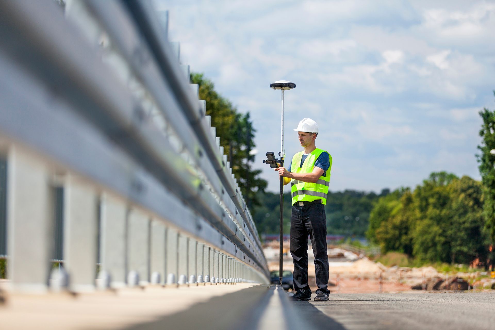 A construction worker is standing on the side of a road using a gps device.