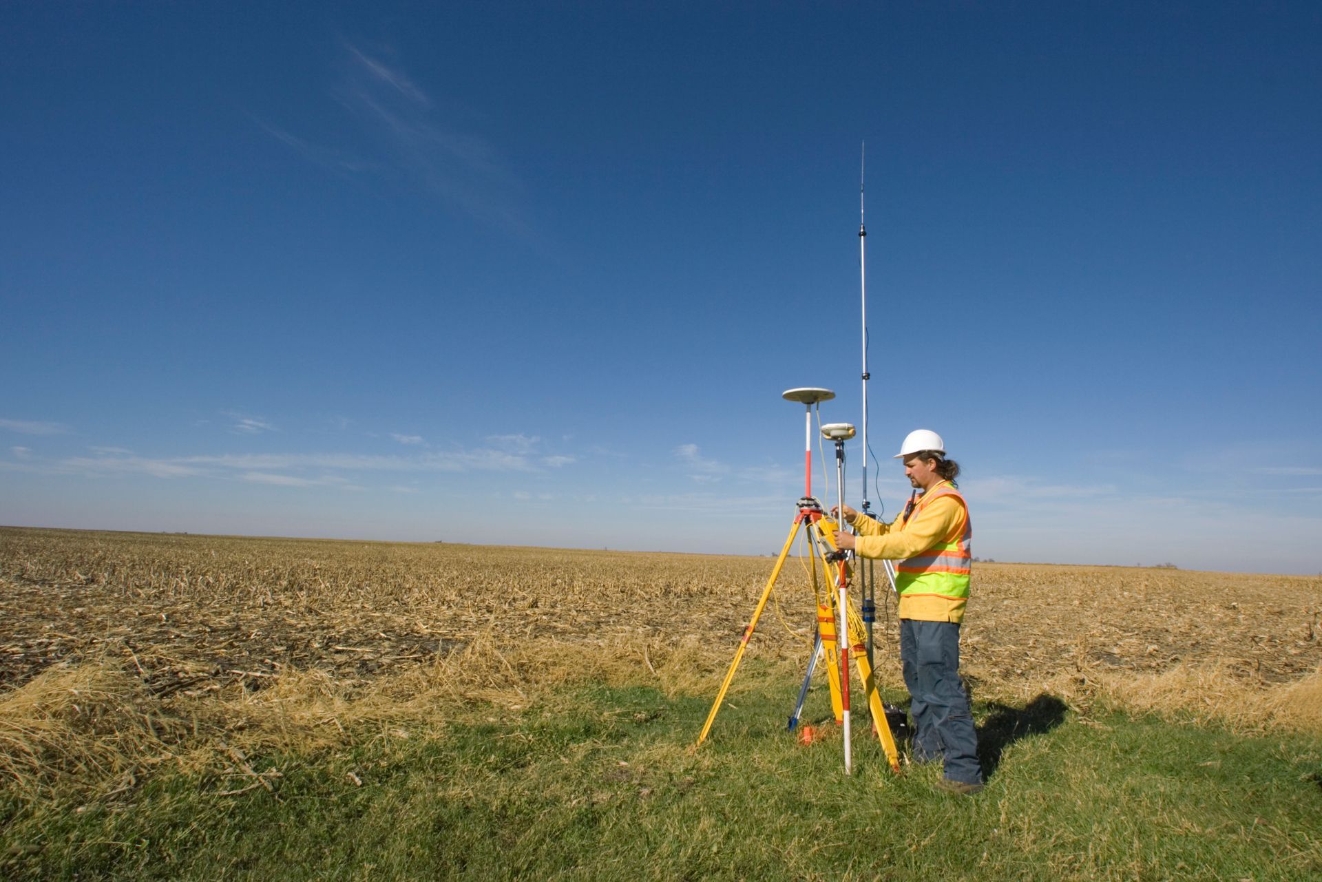 A man is standing in a field with a tripod and a satellite dish.