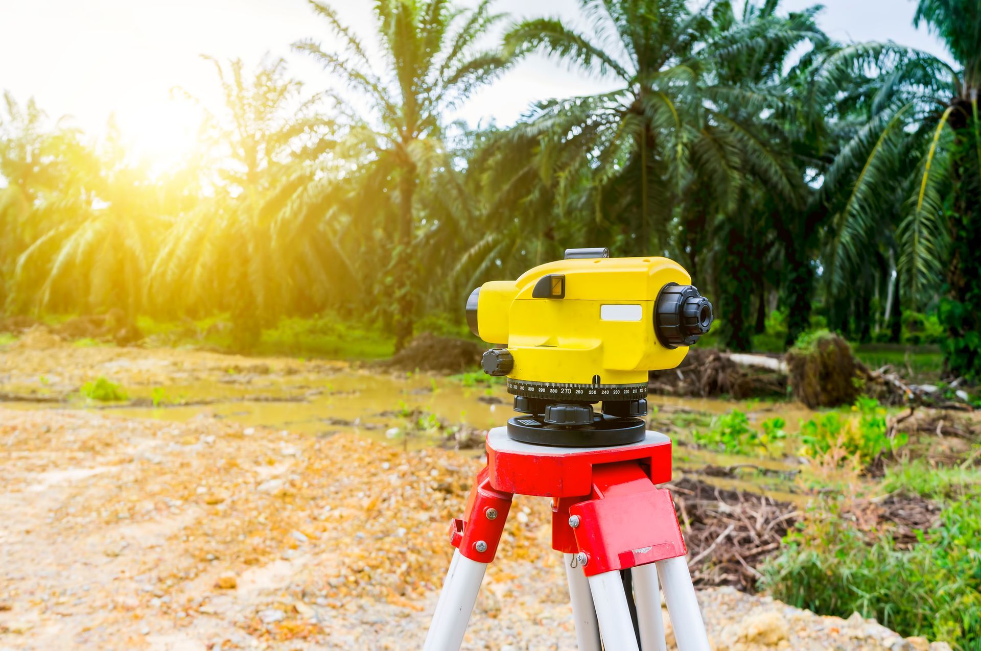 A yellow level is sitting on a tripod in a field.