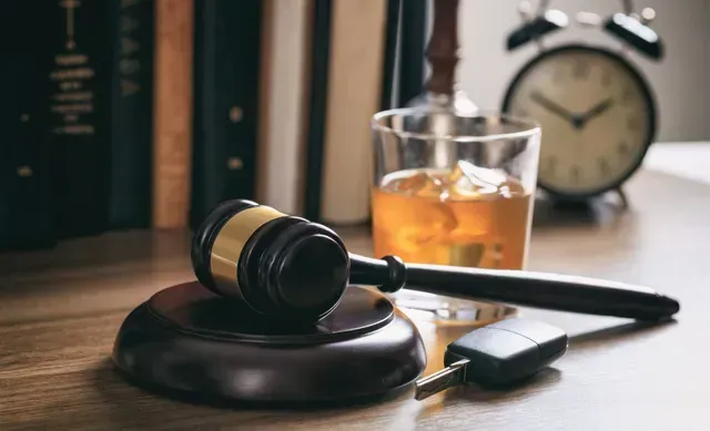 DUI lawyer concept image with judge gavel, whiskey glass, car keys, law books, and clock on desk.