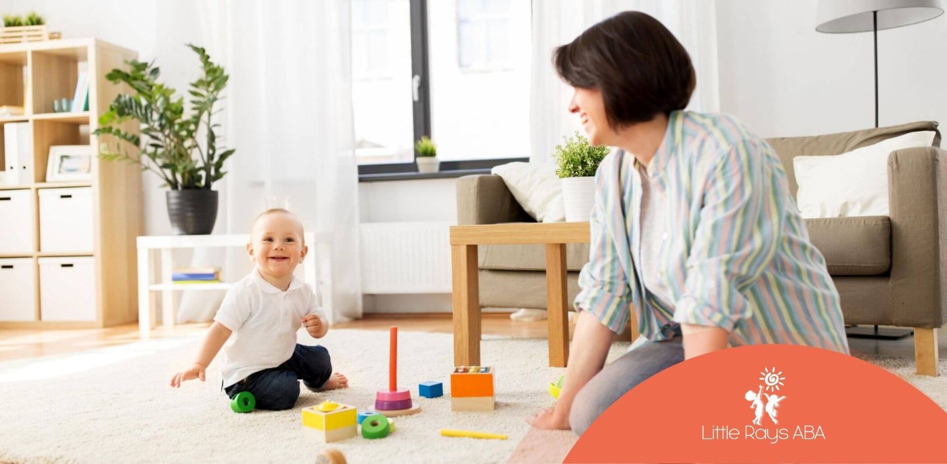 Smiling toddler playing with colorful wooden toys on the floor with an ABA therapist.