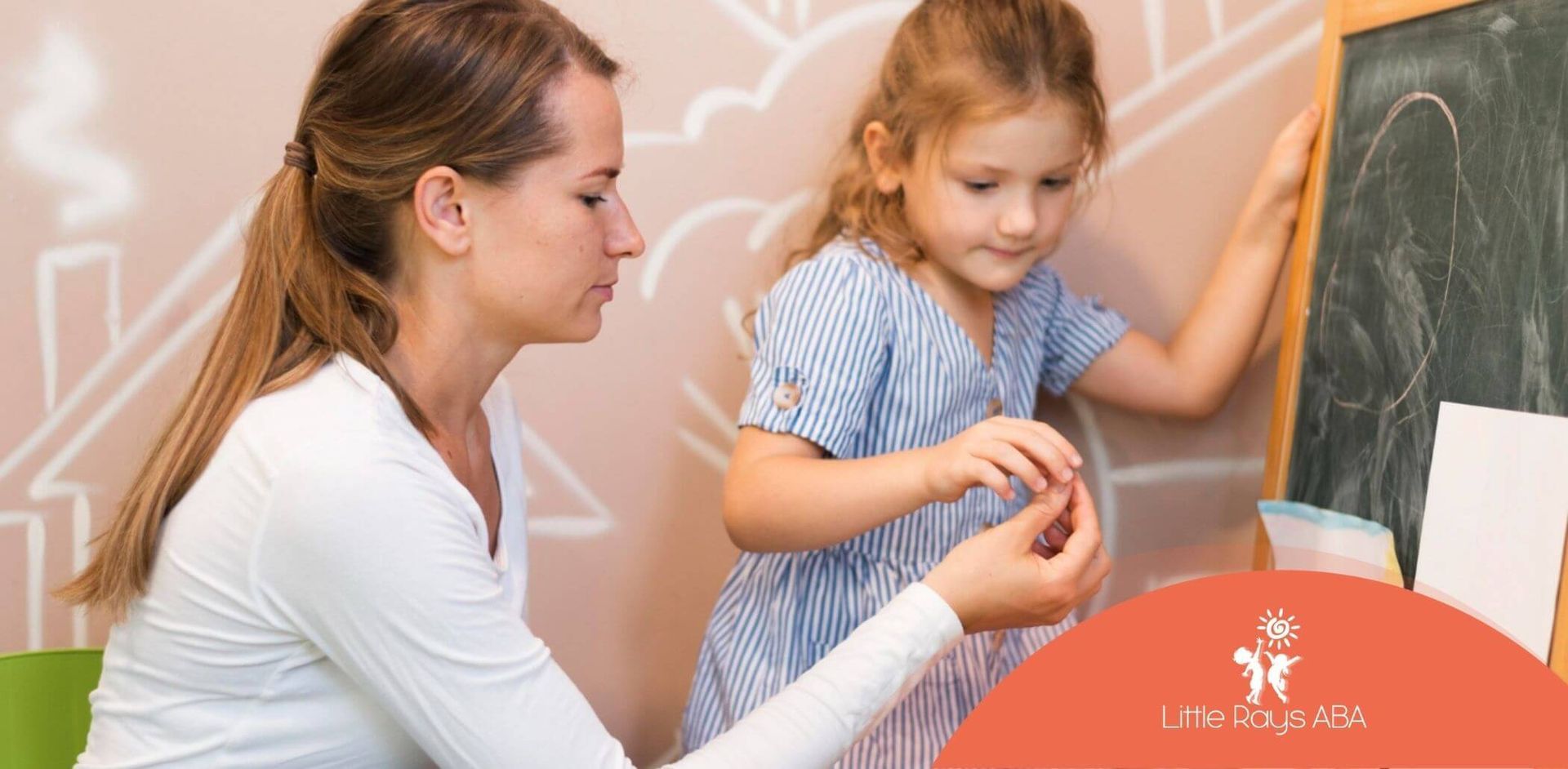 ABA therapist teaching young girl at chalkboard in ABA therapy.