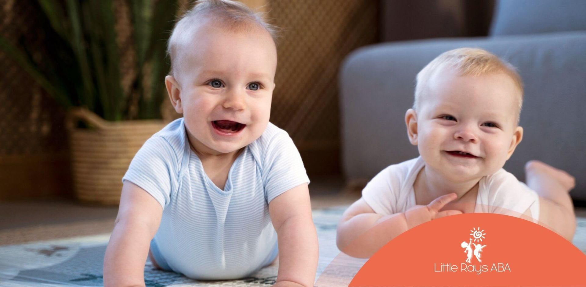 Two babies are laying on the floor and smiling.