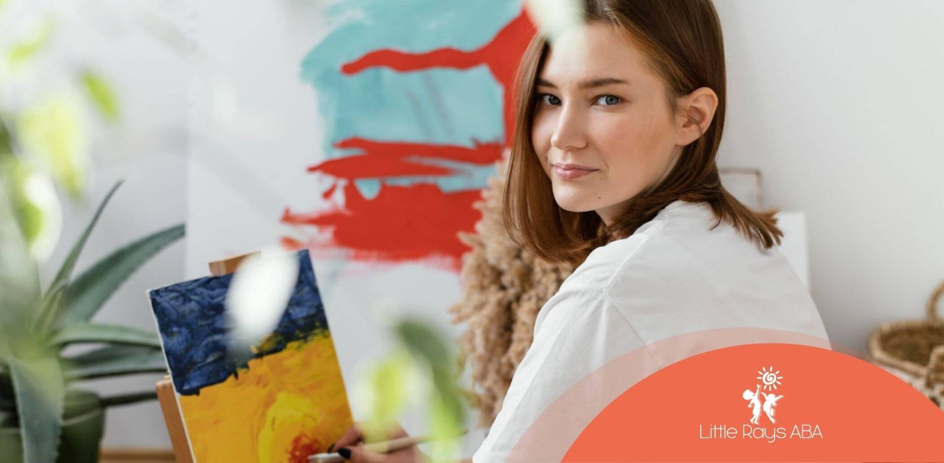 A young woman with autism looking at the camera while painting on a canvas.