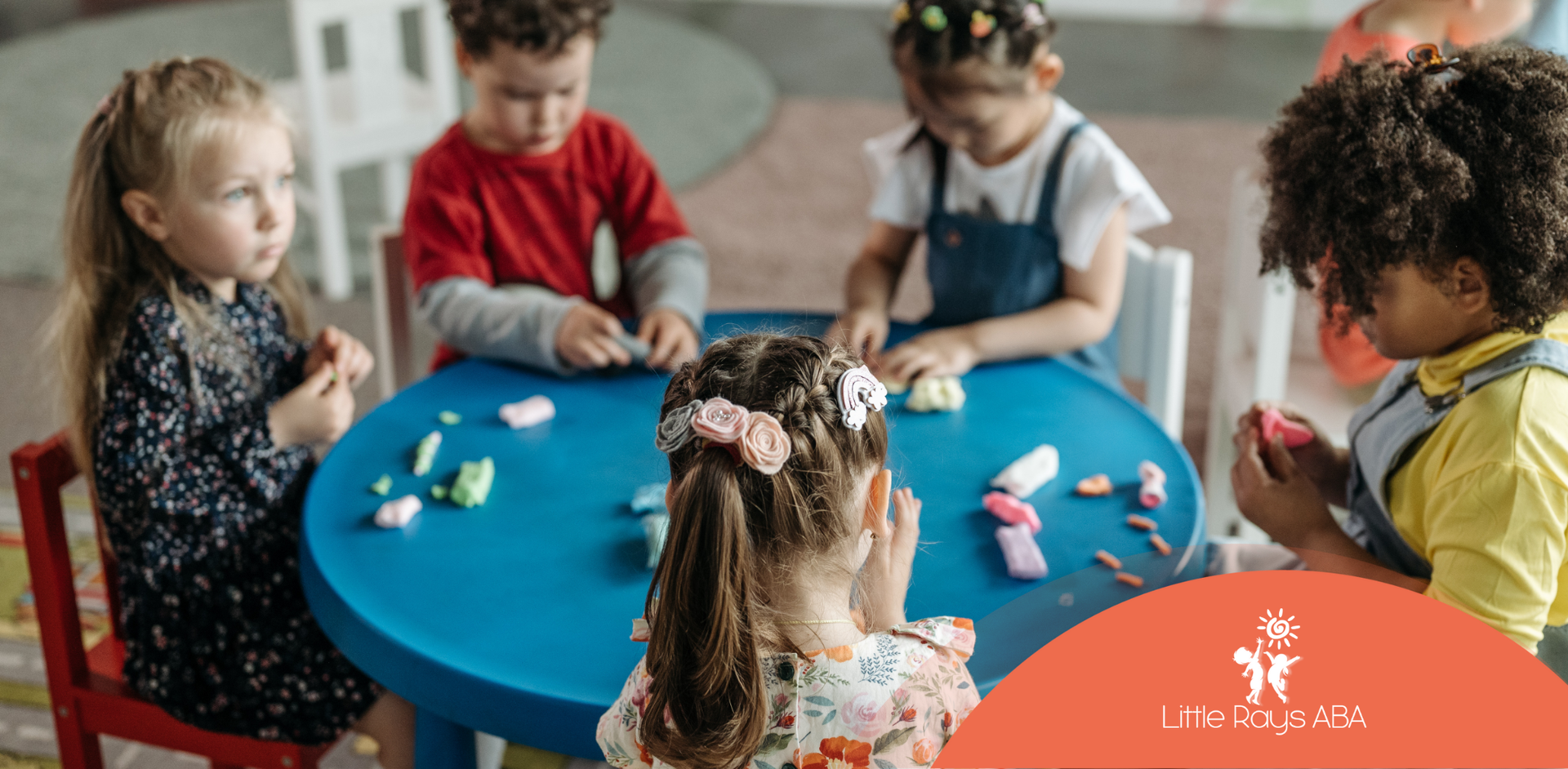 A group of children are sitting at a table playing with clay.