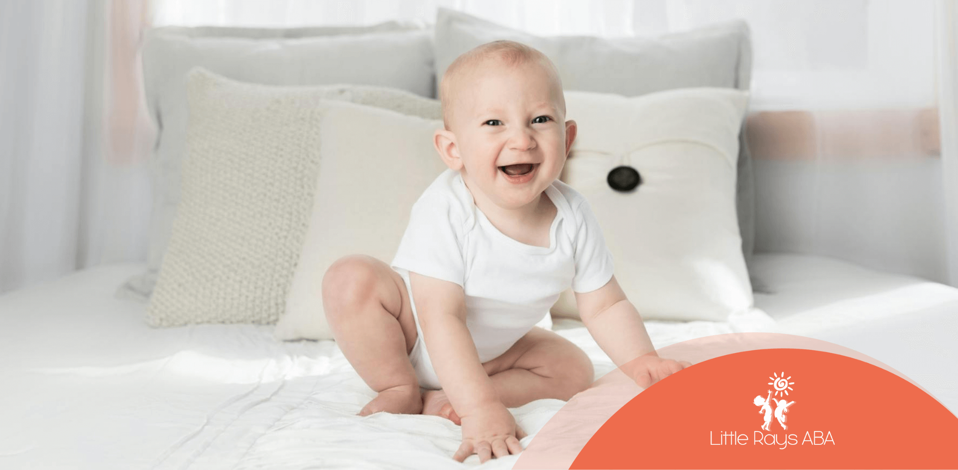 Happy autistic baby sitting on a white bed and smiling during in-home ABA therapy in Florida.