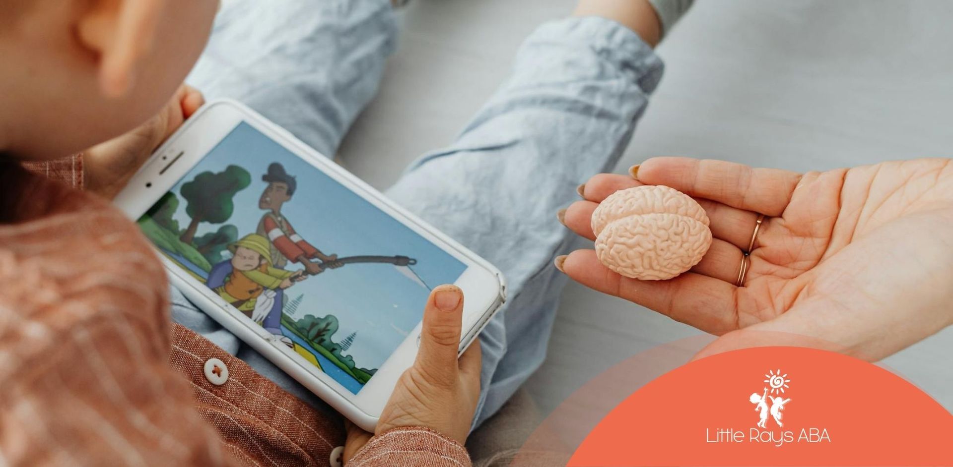 An autistic child watching a cartoon on a smartphone, while an RBT holds a toy brain in Florida.