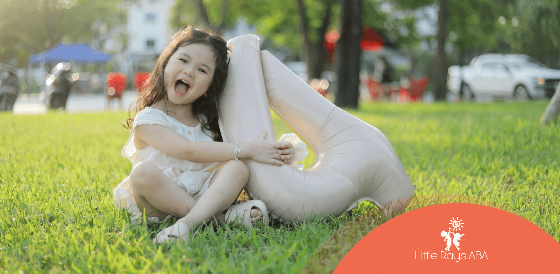 An autistic girl lying on grass with inflatable number 4, smiling and enjoying the outdoors in FL.