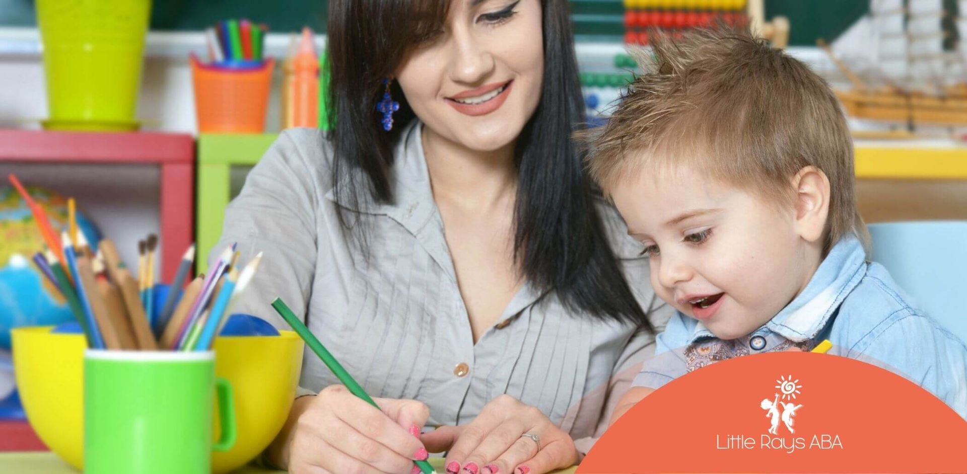 ABA therapist helping young boy with drawing activity at a table in ABA therapy.