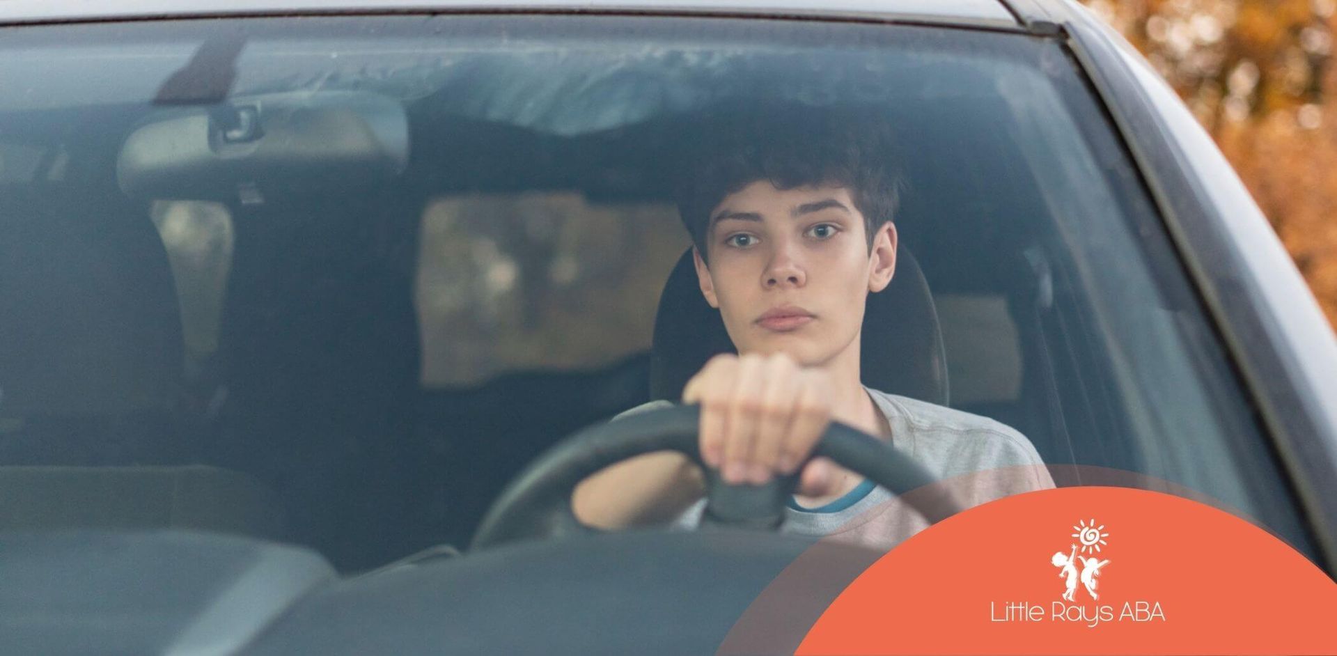 A young man is driving a car and looking at the camera.