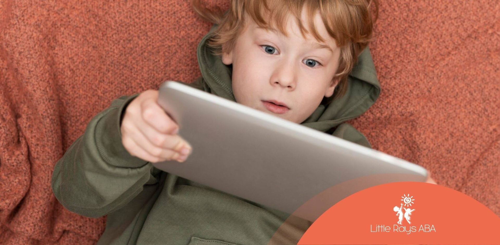 An autistic child lying down while holding an iPad after his in-home ABA therapy.