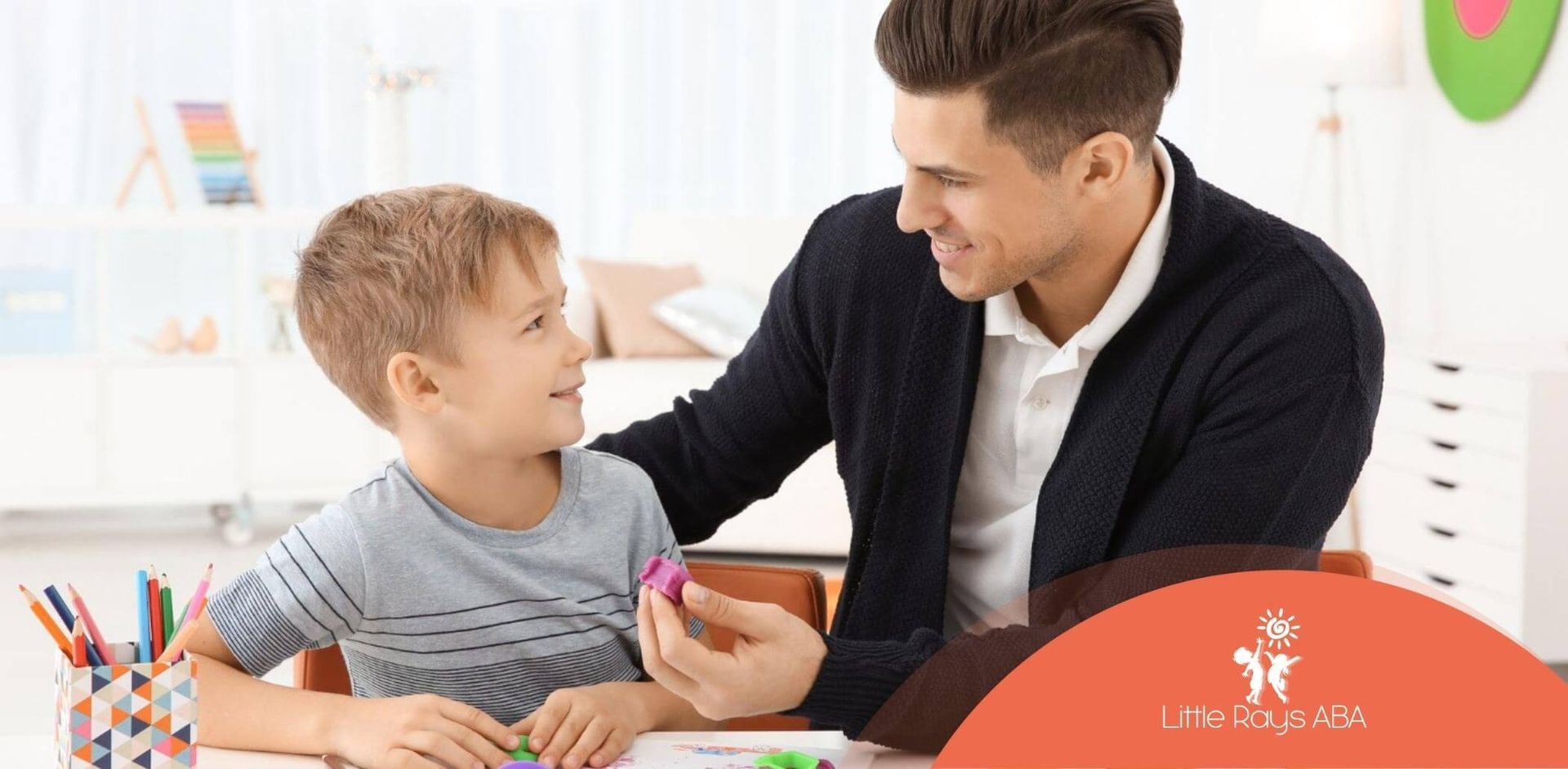 Male ABA therapist working with boy using playdough in classroom.