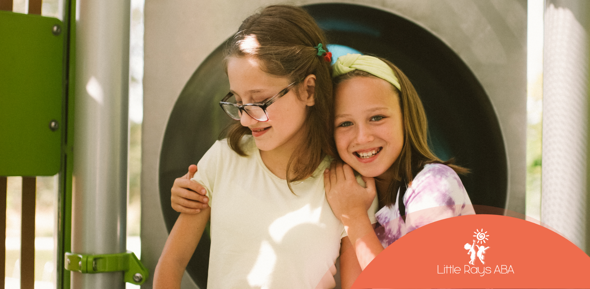 Two young girls are hugging each other on a playground slide.