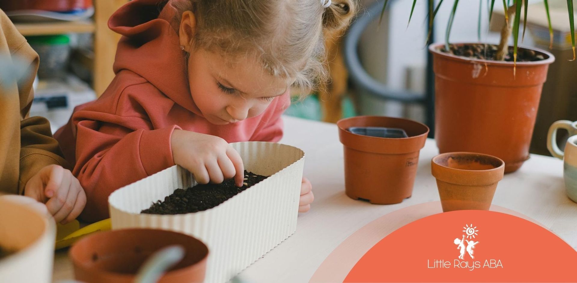 A young autistic child planting seeds in a container, surrounded by small plant pots in Florida.