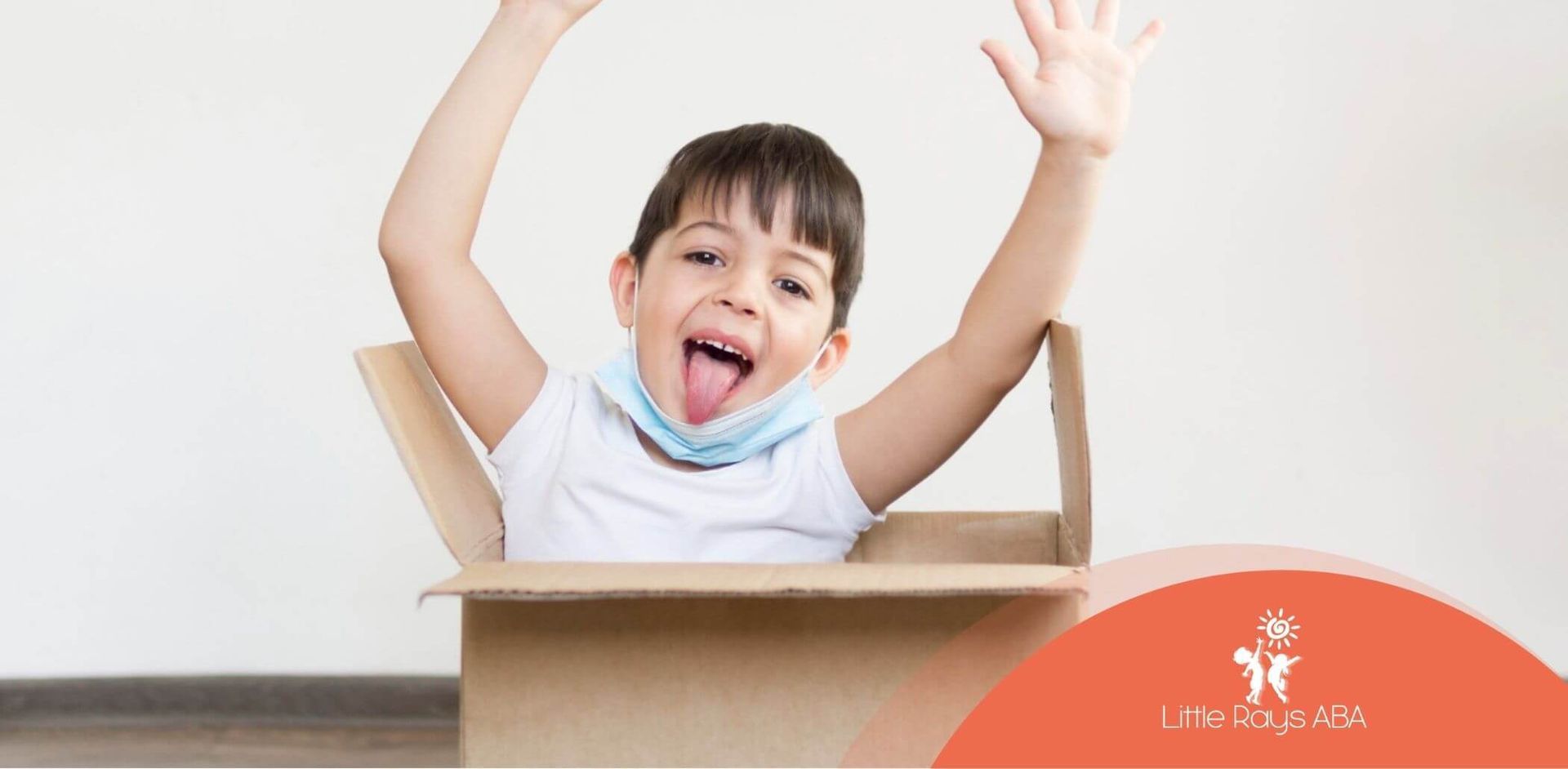 A young boy is sticking his tongue out while sitting in a cardboard box.