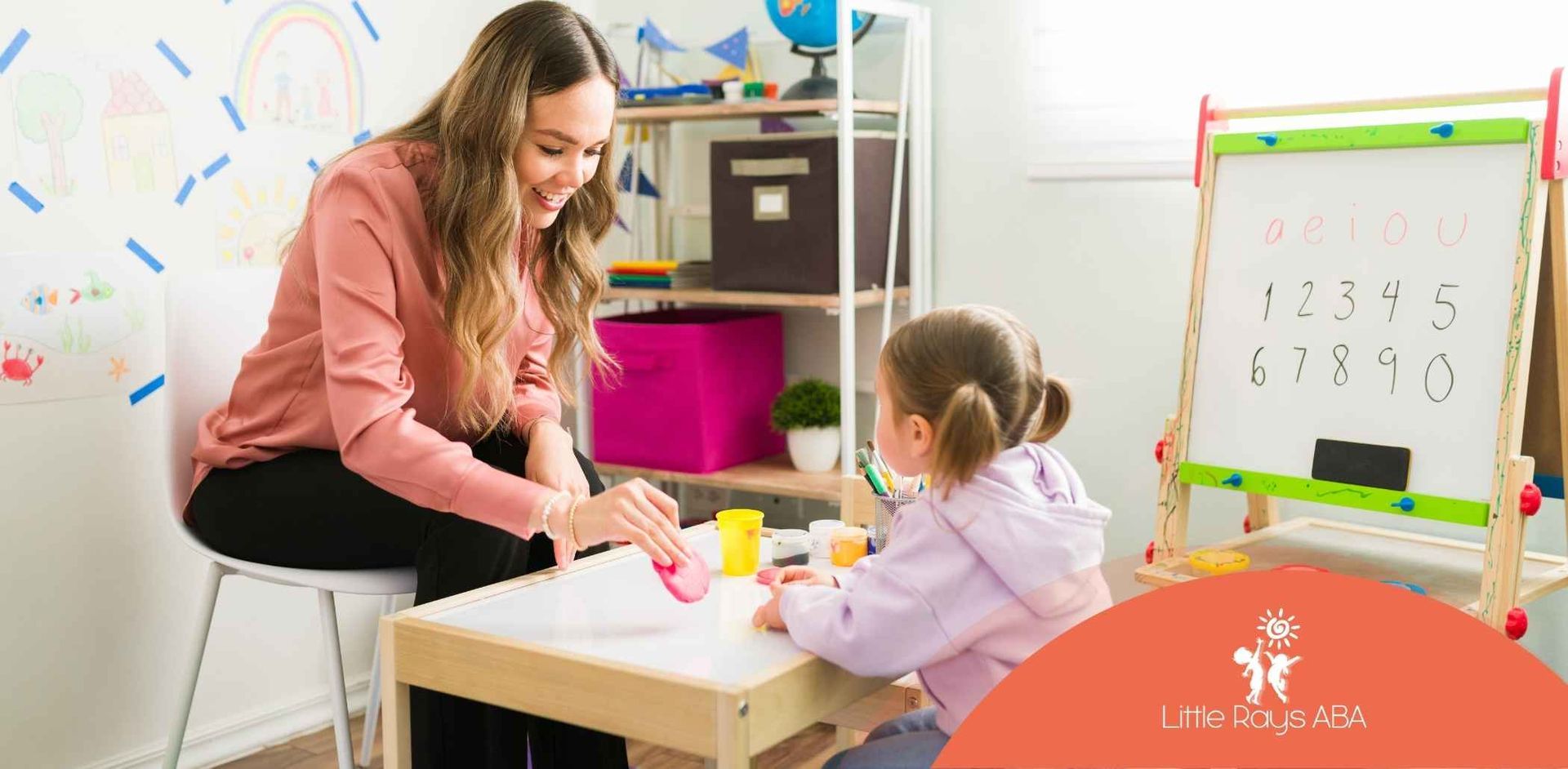 Woman teaching a young girl. They sit at a table with art supplies. A whiteboard with numbers is in the background.