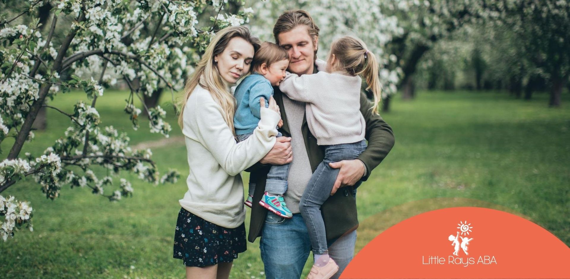 Family of four with autistic children hugging under blooming trees at a spring park in Florida.