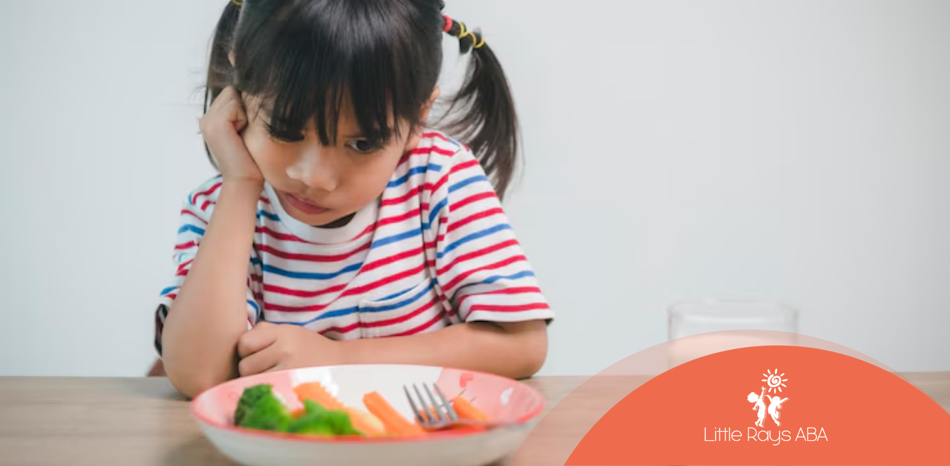 A little girl is sitting at a table looking at a plate of vegetables.