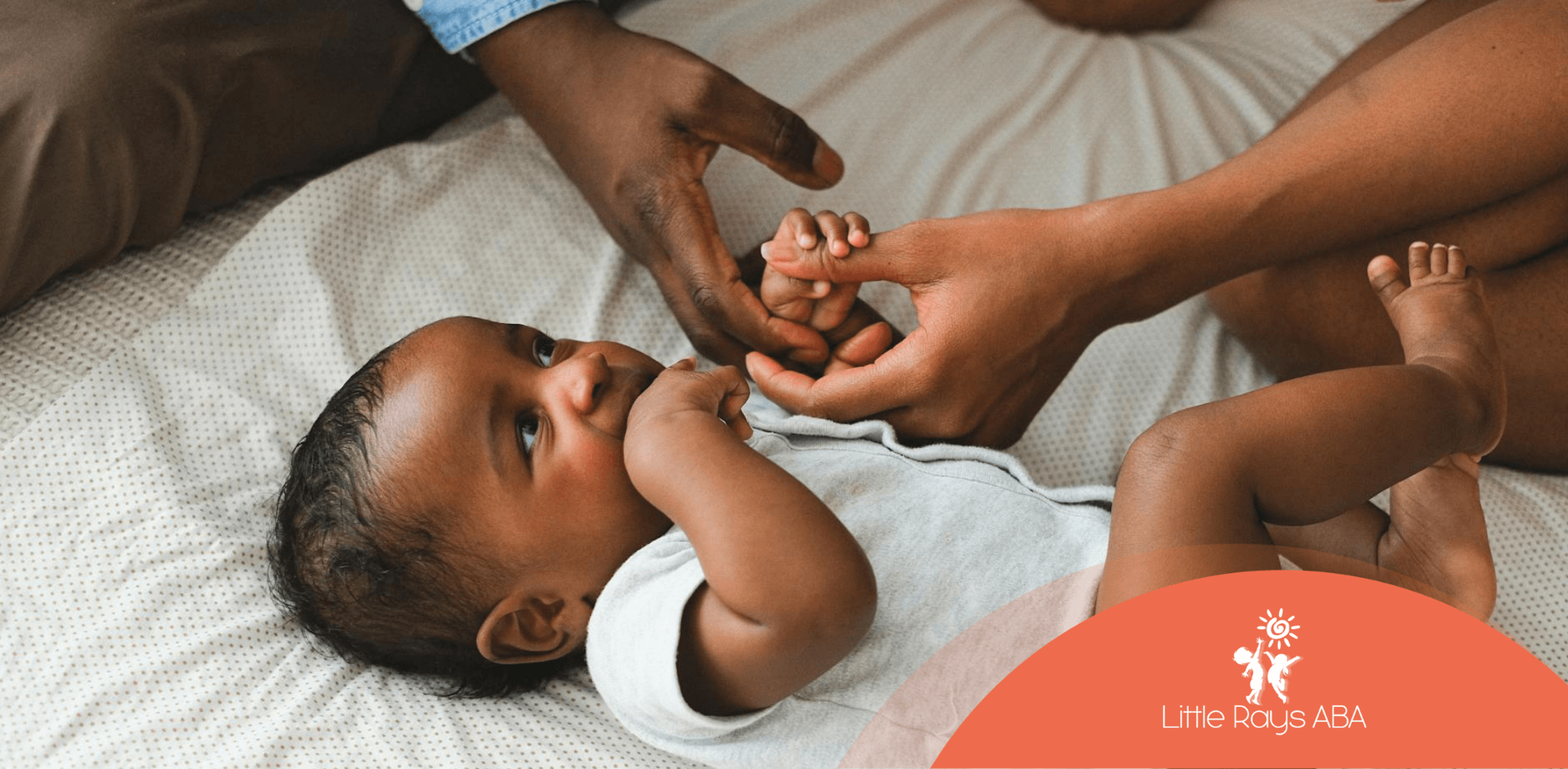 An autistic baby lying on a bed holding a parent’s finger during tactile sensitivity activity in FL.