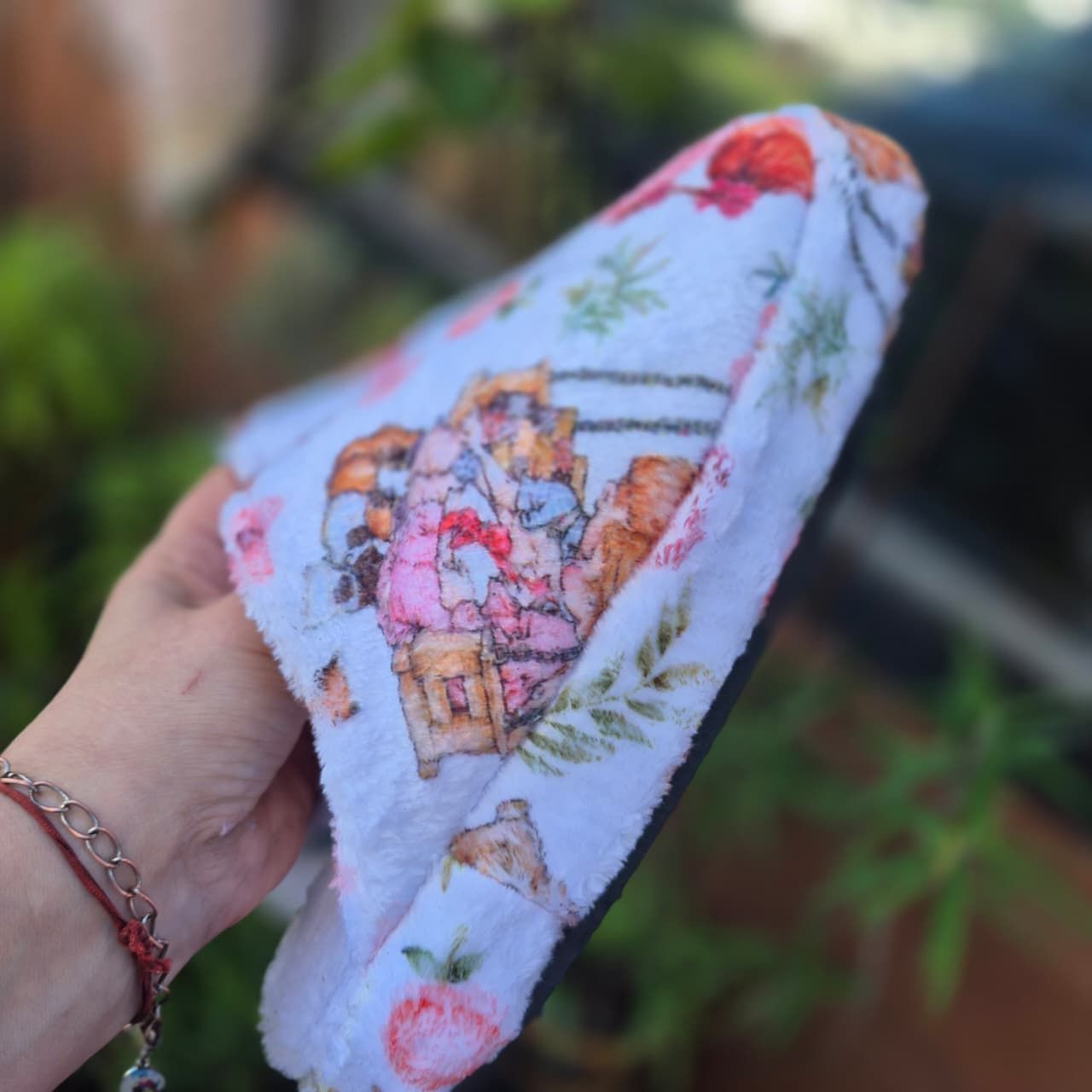Mano sosteniendo manoplas de bebé con estampado floral de flores rosas y mariposas al aire libre