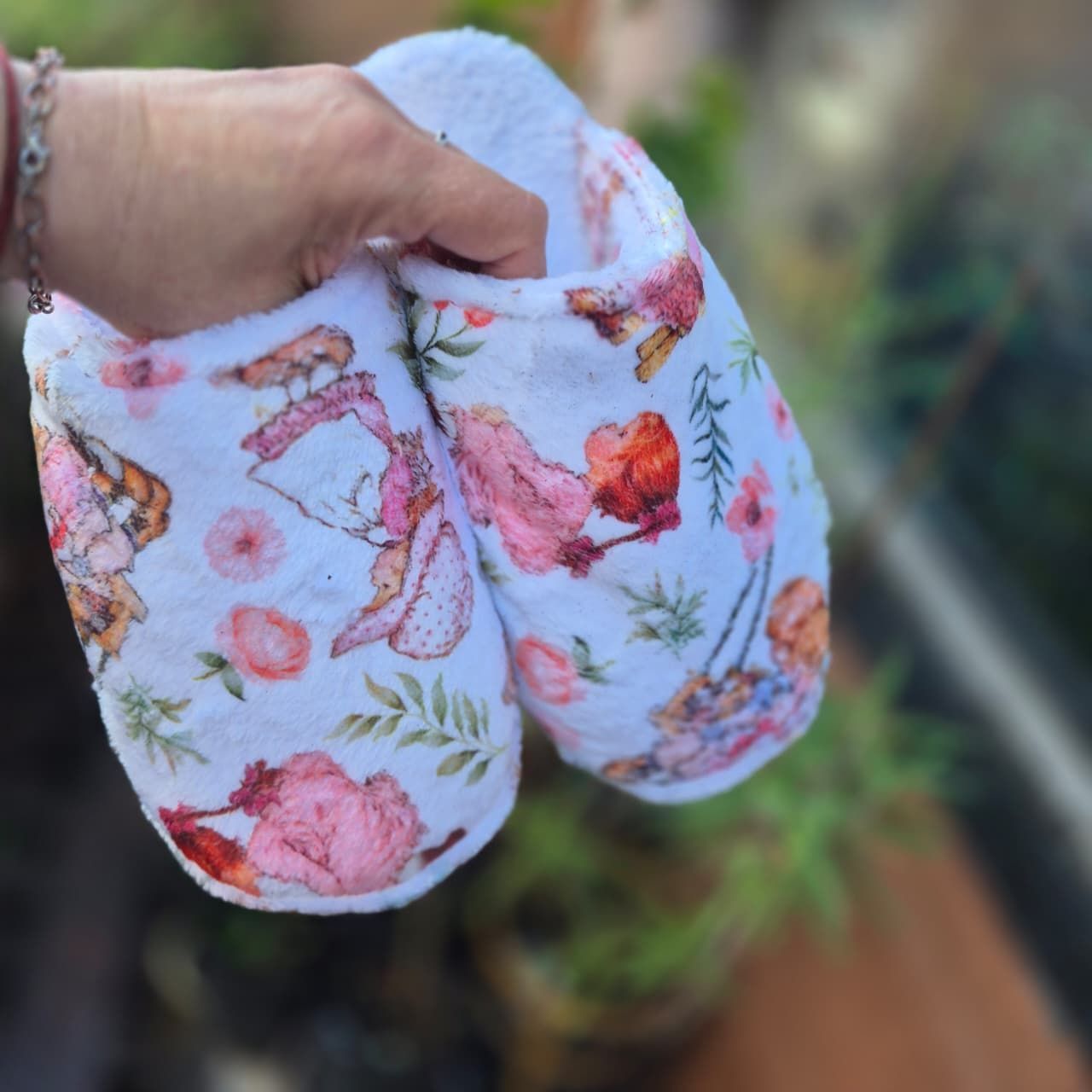 Mano sosteniendo manoplas de bebé con estampado floral de flores rosas y mariposas al aire libre