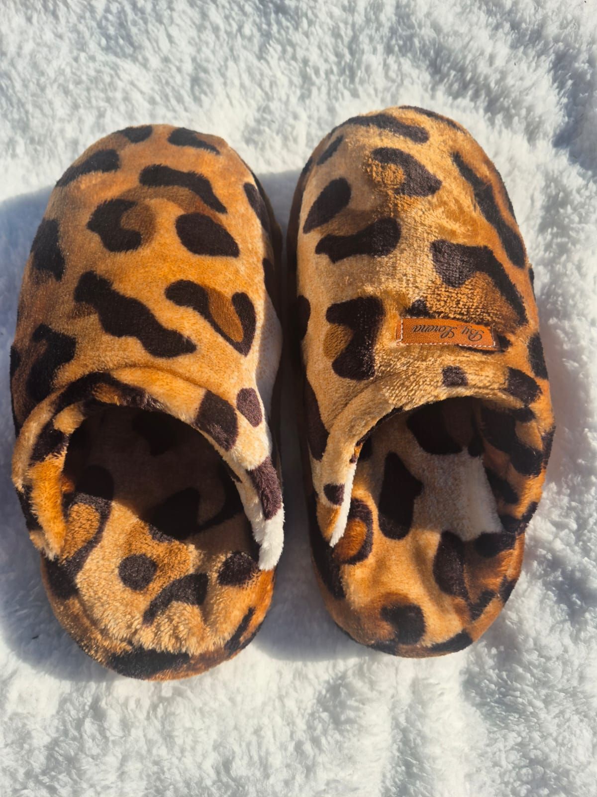 Pantuflas peludas con estampado de leopardo sobre una superficie blanca texturizada.