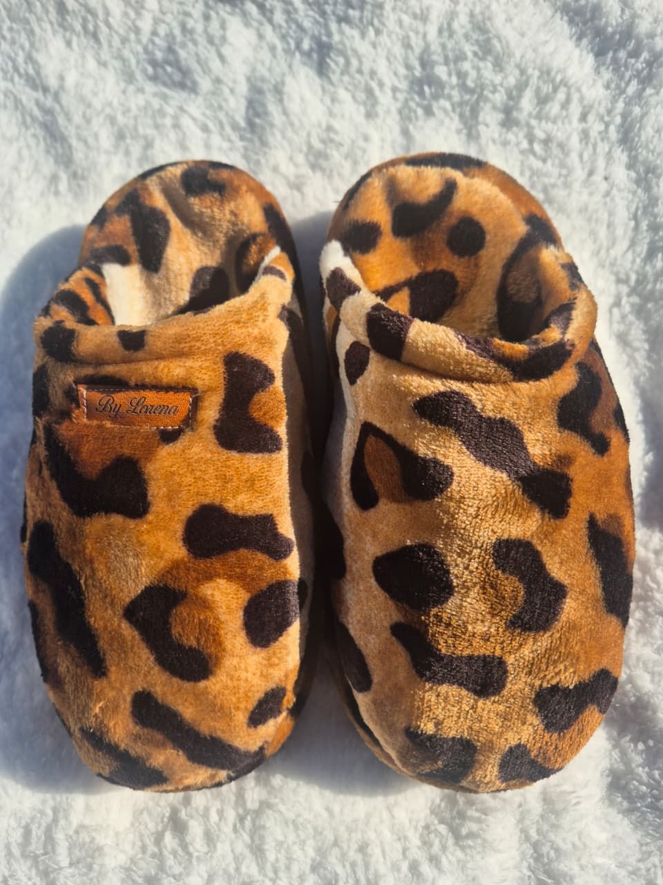 Pantuflas sin cordones con estampado de leopardo sobre una superficie blanca texturizada.