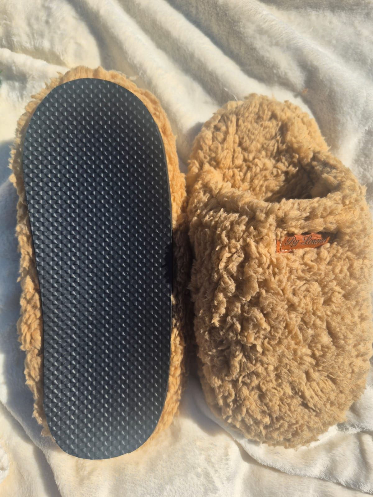 Pantuflas de sherpa color canela y suave, una mostrada de lado y la otra desde arriba, sobre una manta blanca.