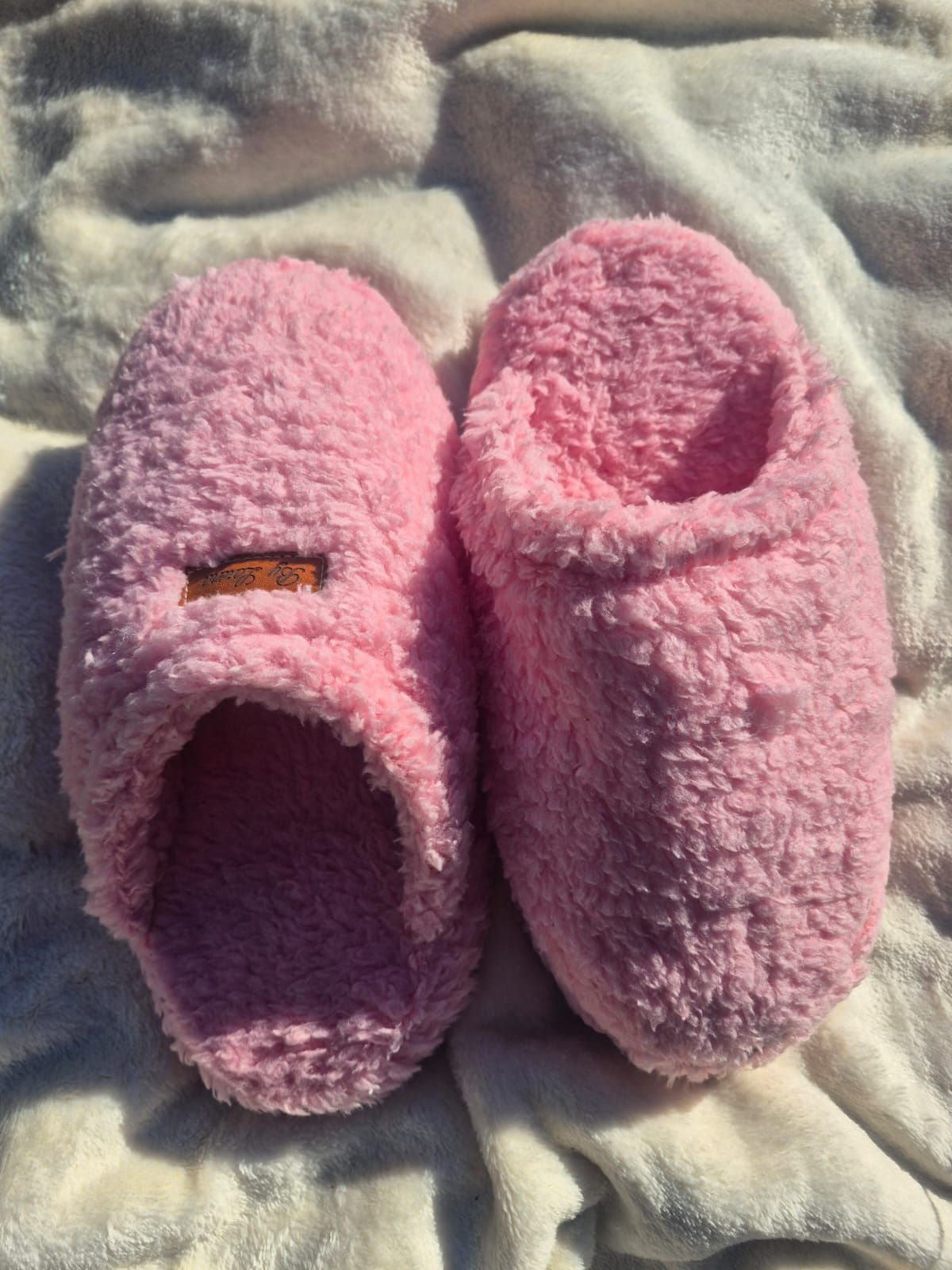 Un par de pantuflas rosas y peludas sobre una suave manta gris.
