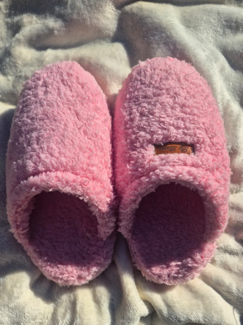 Un par de pantuflas rosas y peludas sobre una suave manta gris.