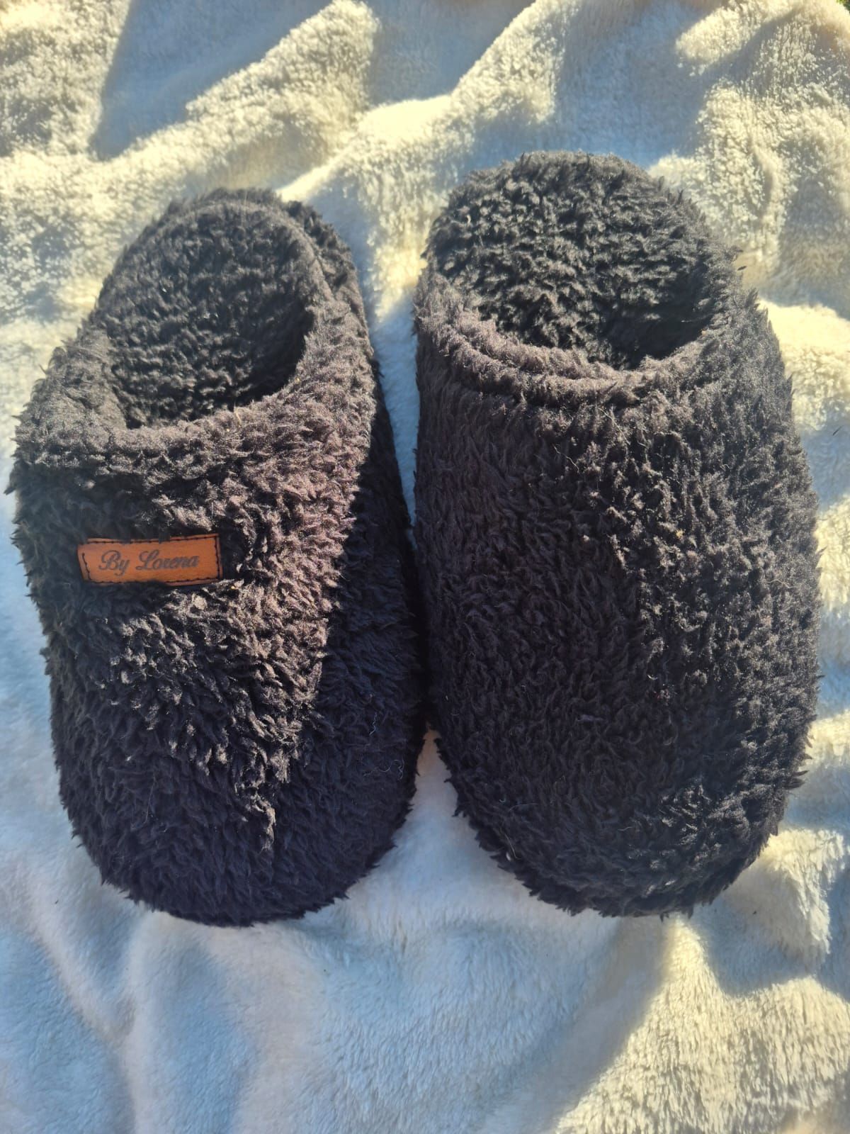Un par de pantuflas negras de felpa, una de ellas con suela negra de relieve texturizado.