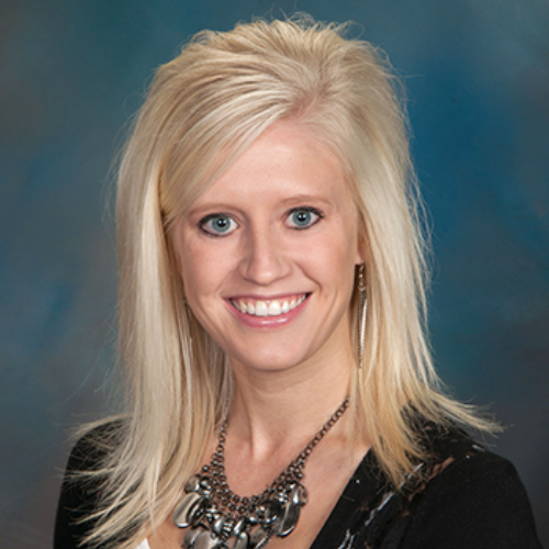 A woman wearing a black sweater and a necklace is smiling for the camera.