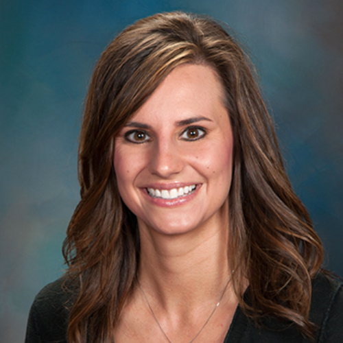 A woman wearing a black jacket and a white shirt is smiling for the camera.