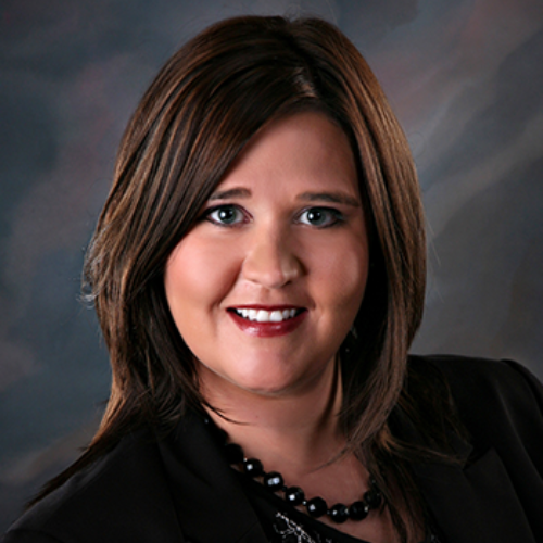 A woman wearing a black jacket and a necklace smiles for the camera