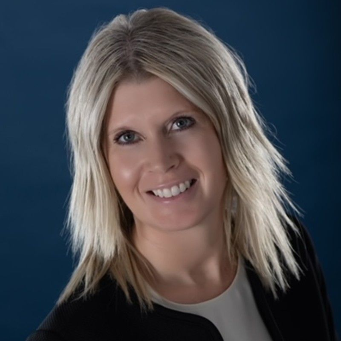 A woman with blonde hair is wearing a black jacket and smiling.