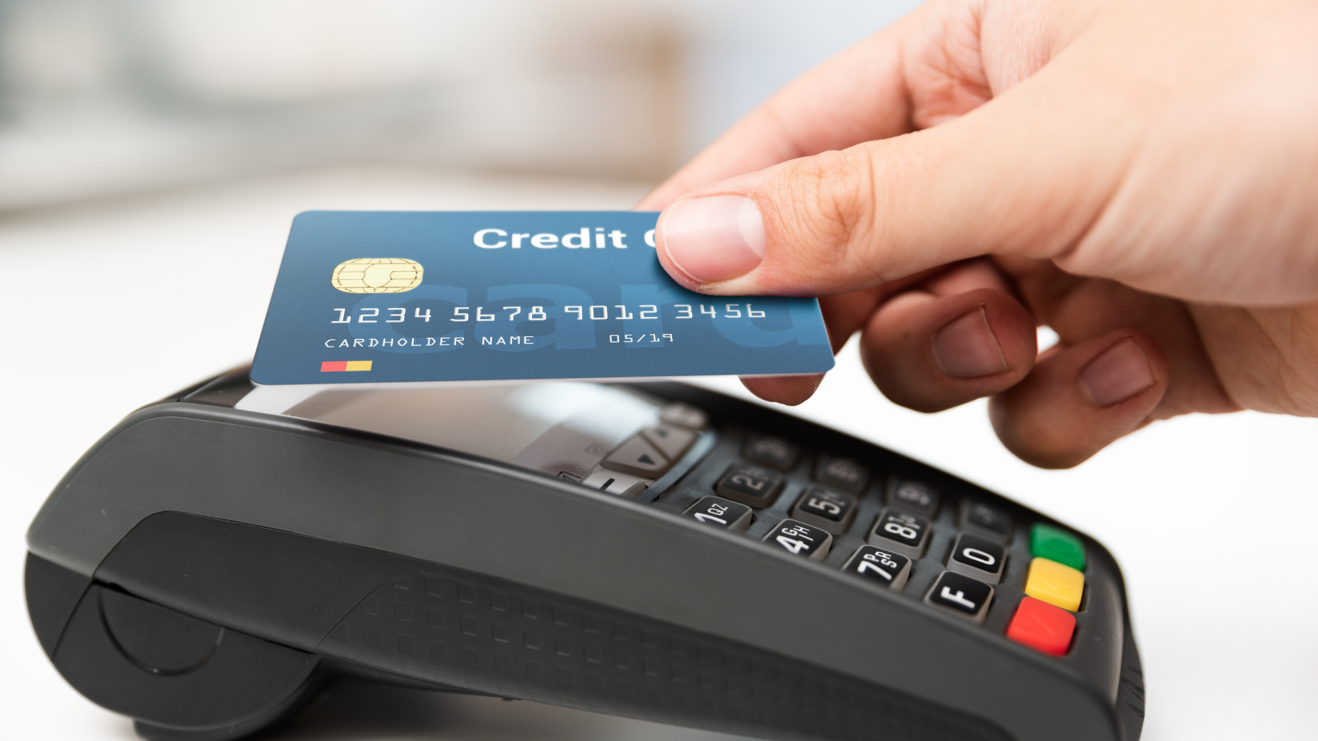 A person is holding a credit card over a credit card reader.