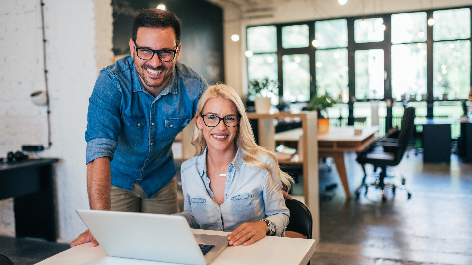 A man and a woman are standing next to each other in front of a laptop computer.