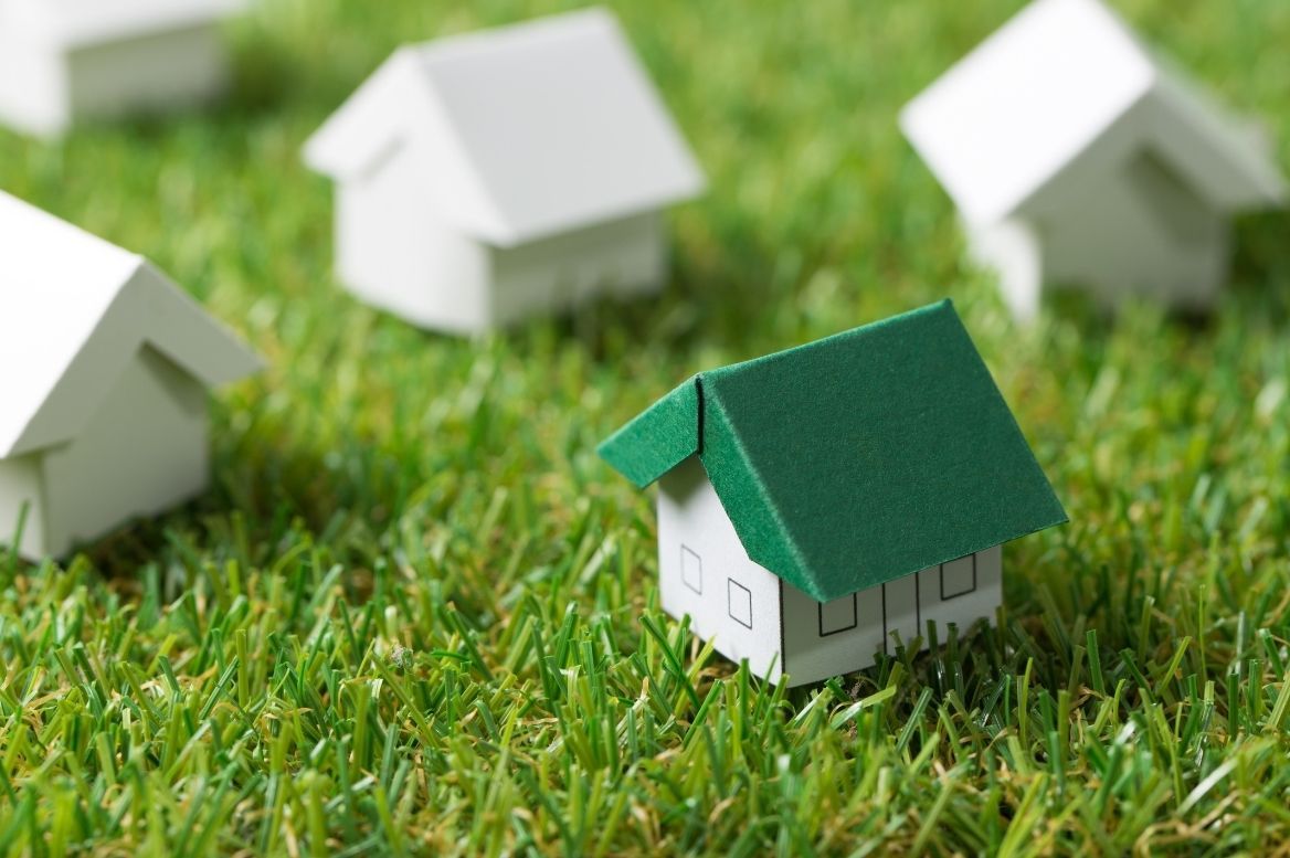 A small model house with a green roof is sitting on top of a lush green field.