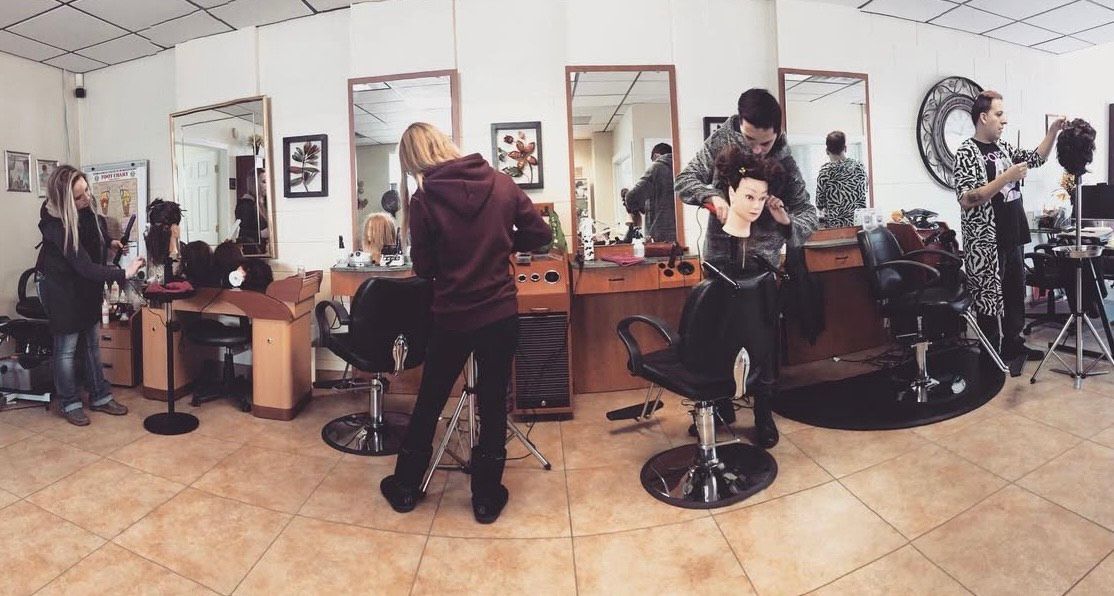 A wide-angle view of a hair salon with stylists and clients, featuring mirrors, cutting chairs, and people interacting.